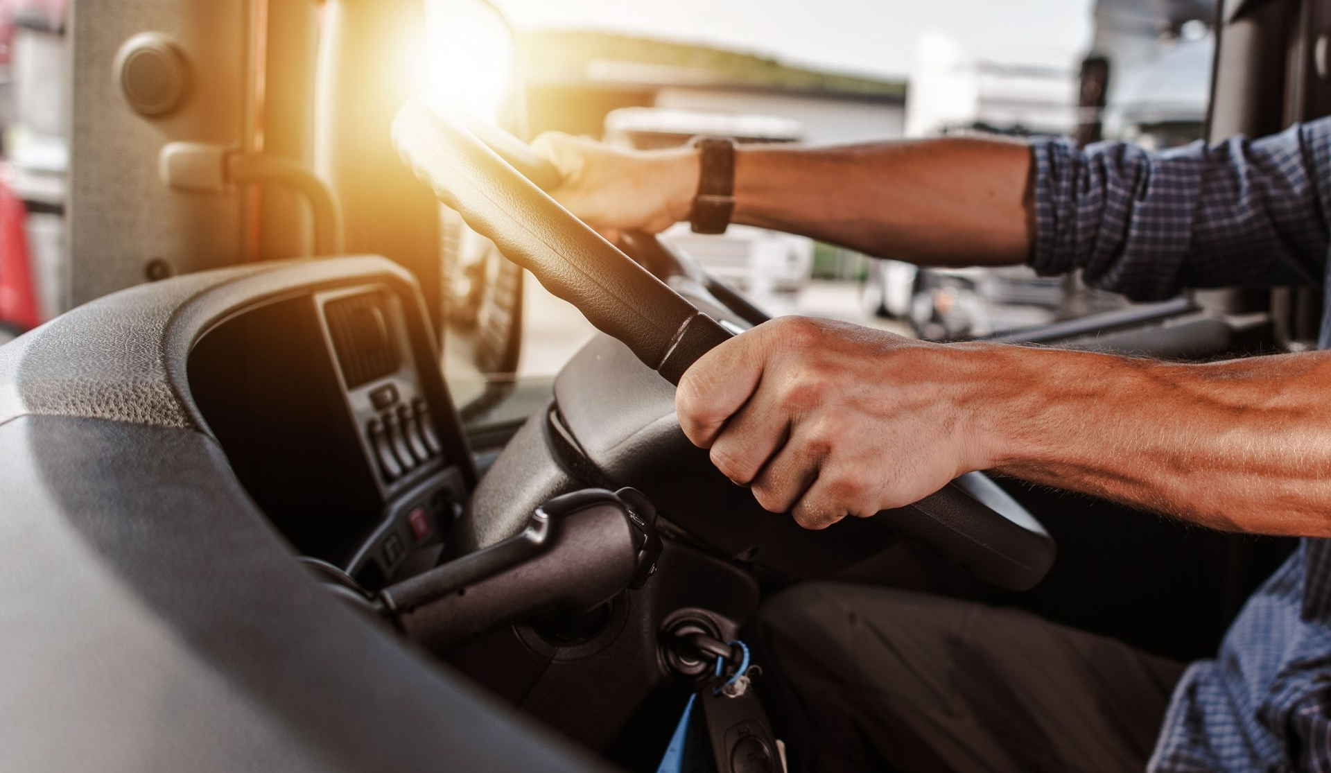 Hands holding a steering wheel in a sunlit vehicle interior, with a dashboard and seat visible.
