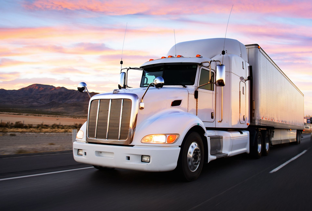 White semi-truck driving on a highway at sunset with mountains in the background