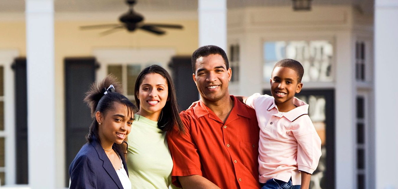 Four smiling people standing together on a porch outside a house