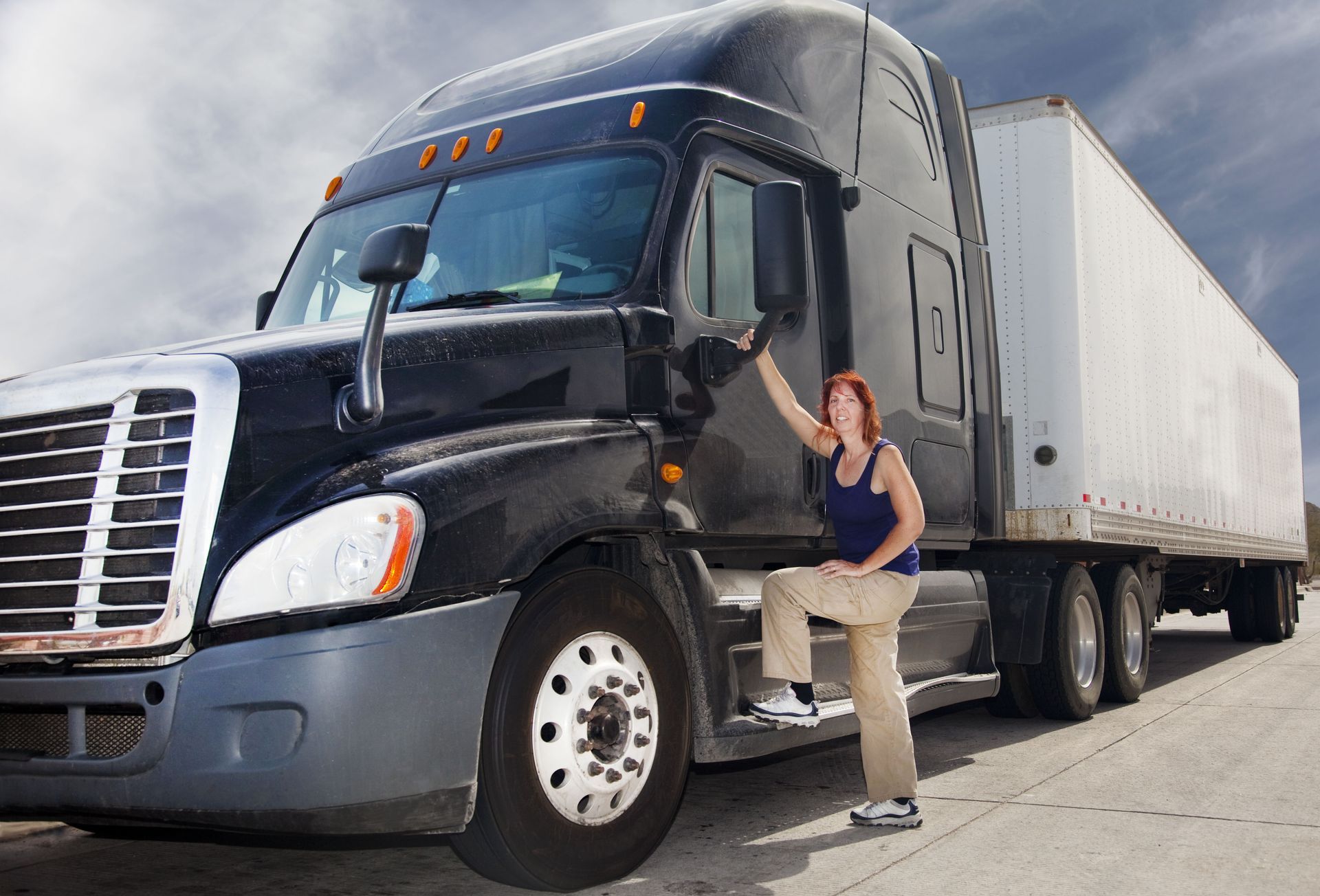 Woman standing beside a black semi-truck and white trailer on a road