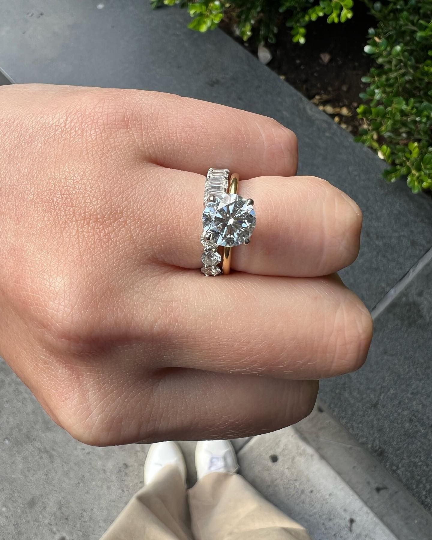 Hand wearing two diamond rings; one with a large round stone, and one with small stones.