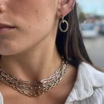 Close-up of a person wearing hoop earrings and a chunky chain necklace.