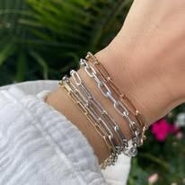 Person wearing a stack of gold and silver chain bracelets on their wrist, with a white sleeve.