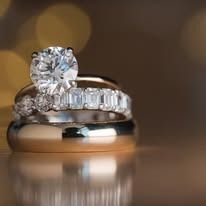 Diamond engagement ring with two wedding bands, reflecting light.