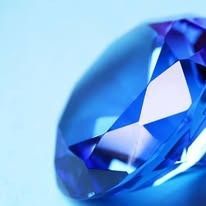 Close-up of a faceted, vibrant blue gemstone, possibly a sapphire, against a light blue background.