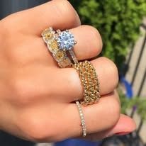 Hand wearing three gold rings, one with a blue gem, two with yellow gems, outdoors.