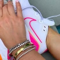 Person's hand with bracelets, next to a white and pink athletic shoe.