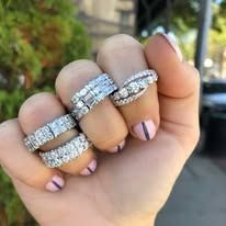 Hand displaying five diamond rings on fingers, against a blurred background.