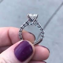 Close-up of a hand holding a sparkling diamond engagement ring with a purple nail.