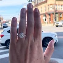 Hand wearing engagement ring with car background.