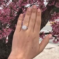 Hand with a diamond engagement ring, pink blossoms in the background.