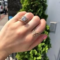 Hand wearing two gold rings with diamonds, in front of greenery.