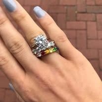 Hand wearing engagement ring with large diamond and a rainbow gemstone band.