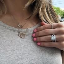 Woman wearing necklaces and rings, pink nail polish, gray top.
