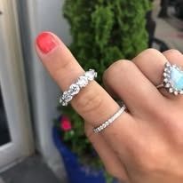 Hand wearing multiple rings: floral design, thin band, and a heart-shaped opal.