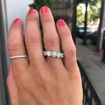Hand with two rings: one thin band, one with round stones, outdoors with railing.
