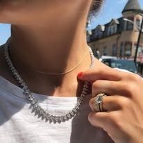 Woman wearing diamond necklace and ring, outdoors.