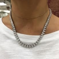 Woman wearing a diamond necklace over a light-colored top, gold chain visible.