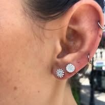 Close-up of a person's ear with multiple silver earrings, including a hoop and studs.