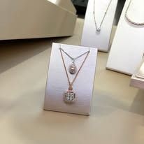 Two necklaces on a white display. One is a diamond teardrop, the other has a square diamond pendant.