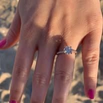 Hand wearing a diamond engagement ring, pink nail polish, outdoors.
