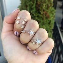 Hand wearing multiple star-shaped silver rings, posed in front of a green bush.