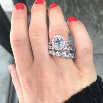 Hand with red nails, wearing a large diamond engagement ring and a diamond wedding band.