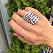 Hand wearing multiple diamond rings against a green backdrop.