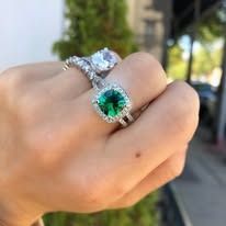 Hand wearing two diamond rings, one with a large green gemstone.