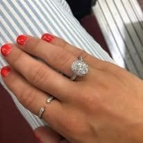 A hand with a large diamond ring on the ring finger, resting on a striped background.
