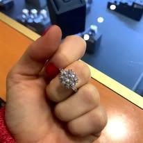 Person's hand wearing a sparkling, multi-stone ring. Finger is resting on a glass surface.