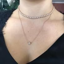 A woman's neck wearing two delicate necklaces with white stones. The top necklace is a choker.