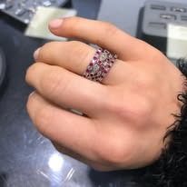 Person's hand wearing a ring with red stones and clear stones.