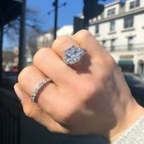 Hand wearing two diamond rings outdoors; one large, square cut, one thin band.