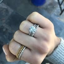 Hand with three diamond rings: engagement ring, wedding band, and stackable band.