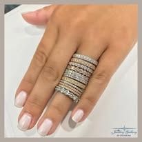 Hand wearing multiple diamond and white gold rings on a white surface.