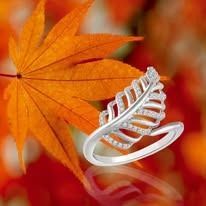 Silver leaf-shaped ring with tiny diamonds beside an orange fall leaf, on a blurred orange background.