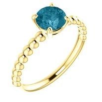 Gold ring with a round, blue gemstone and a beaded band.