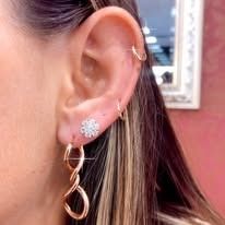 Close-up of a woman's ear wearing gold earrings, including a small flower stud and a looped drop.