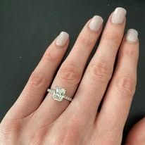 Person's hand with a diamond ring; close-up shot. Focus on the ring's square-cut diamond on a gold band.
