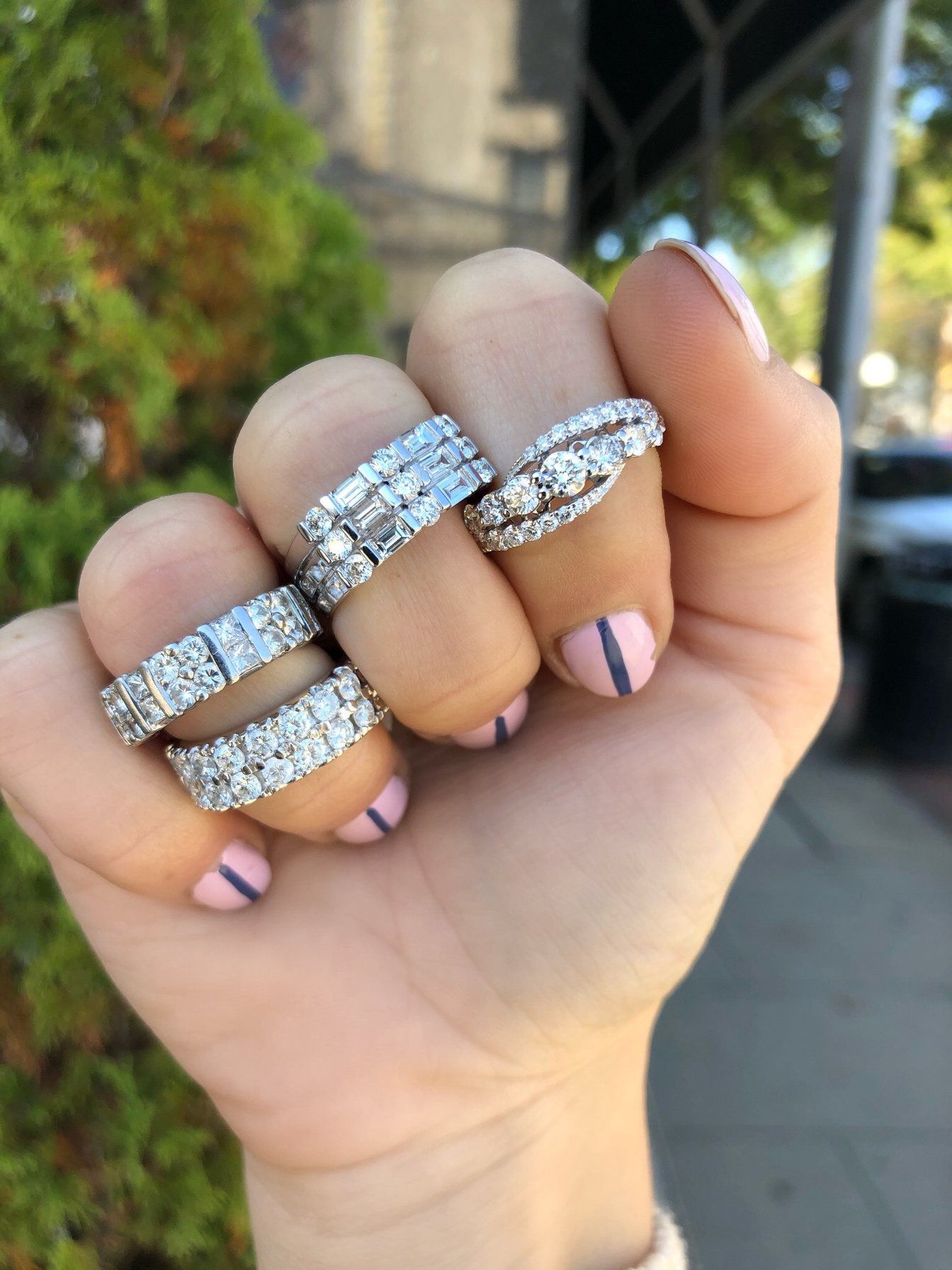 Hand displaying multiple diamond rings with pink nail polish and purple accent stripes.