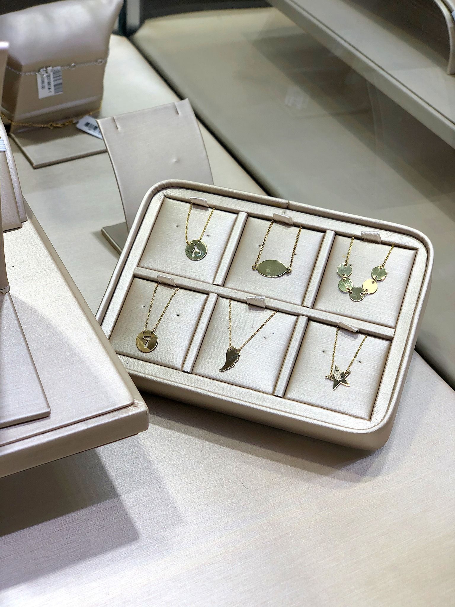 Gold necklaces in a display case. Beige background, small animal pendants.