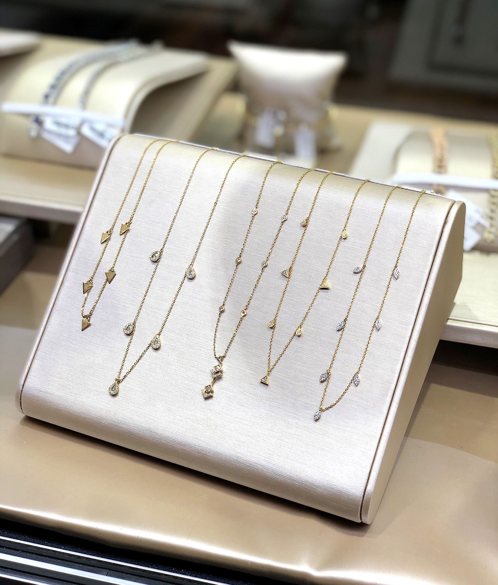 Gold necklaces with small gems displayed on a beige jewelry stand in a store.