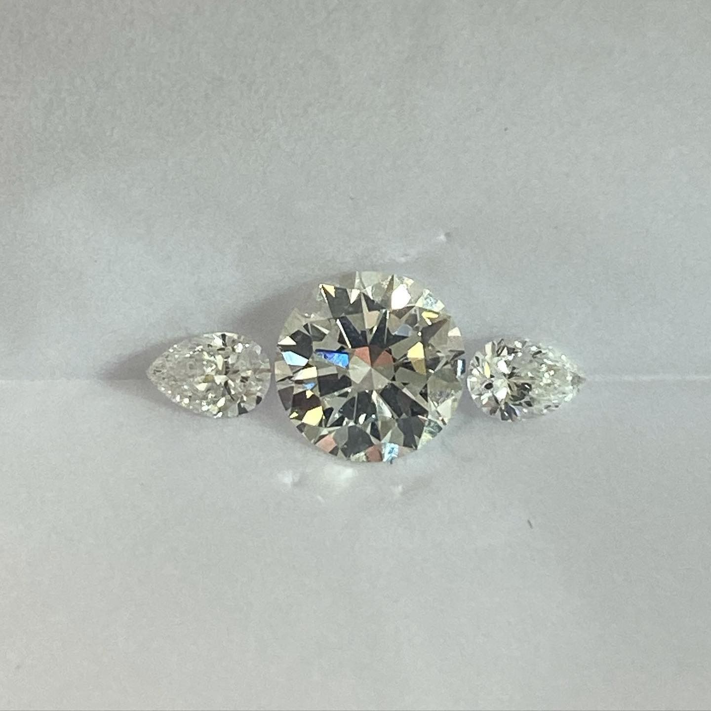 Three clear diamonds: a round center stone flanked by pear-shaped side stones, on a white surface.