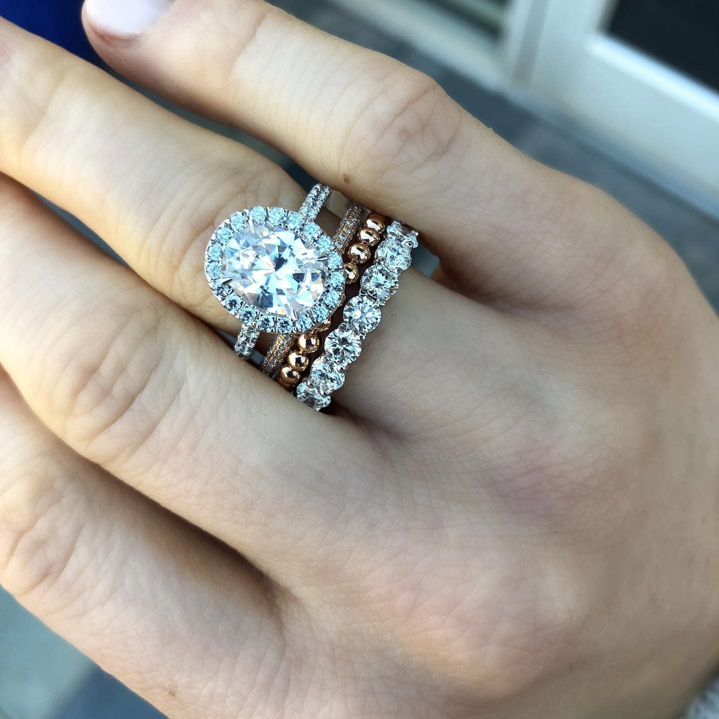 Hand wearing several diamond rings, including an oval engagement ring.