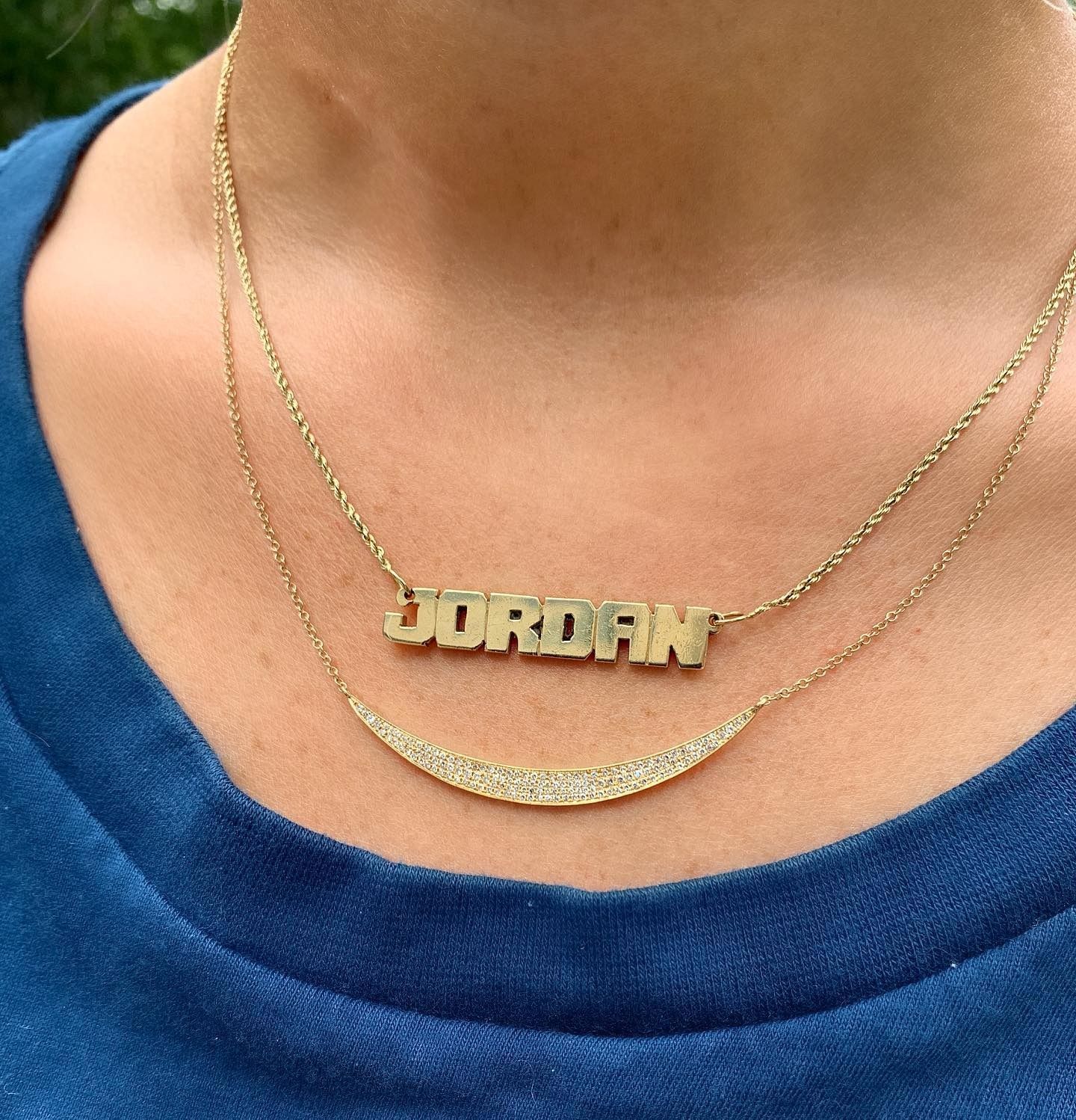 Woman wearing two gold necklaces; one with the name 