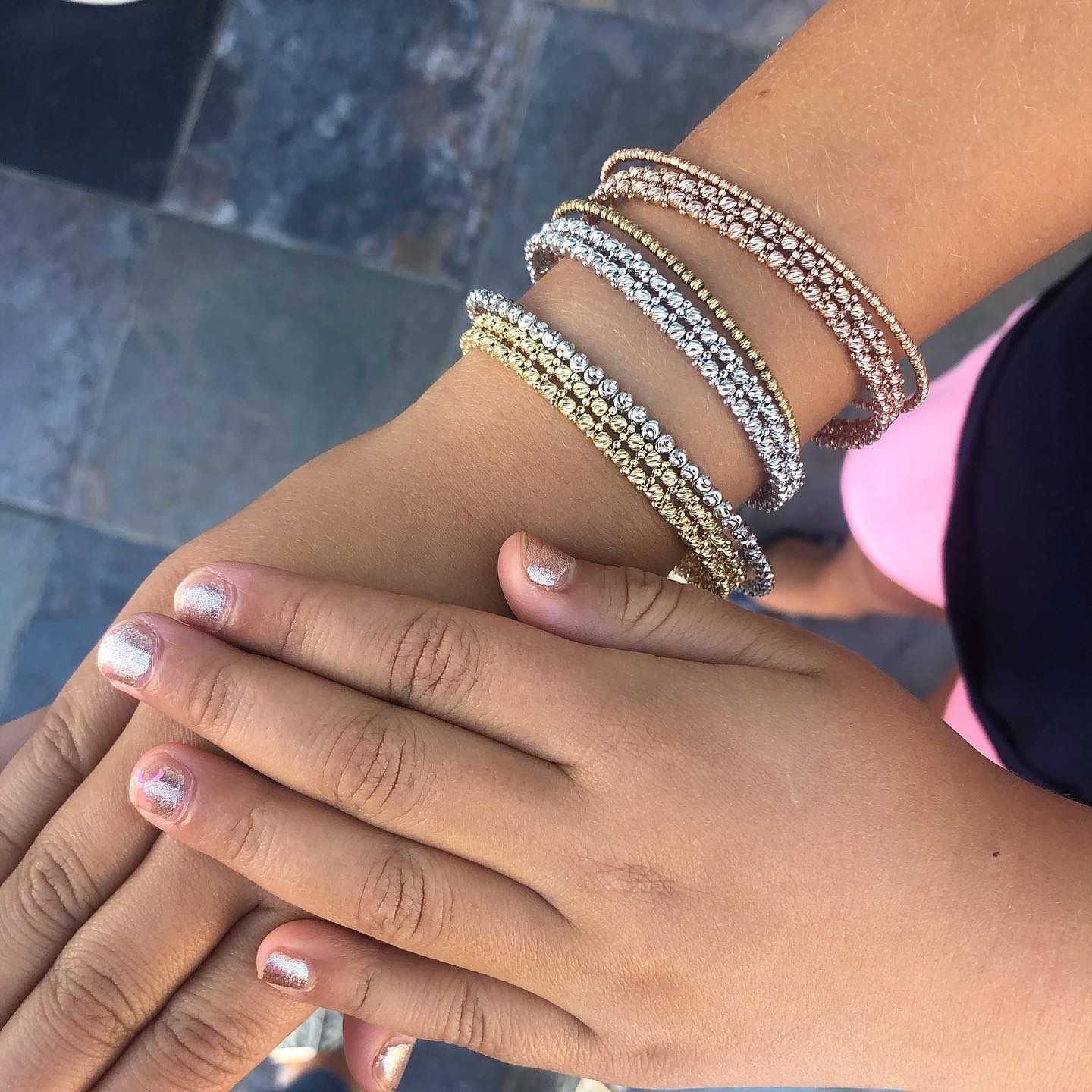 A hand wearing four gold and silver bangles, with painted nails, resting near a body of water.