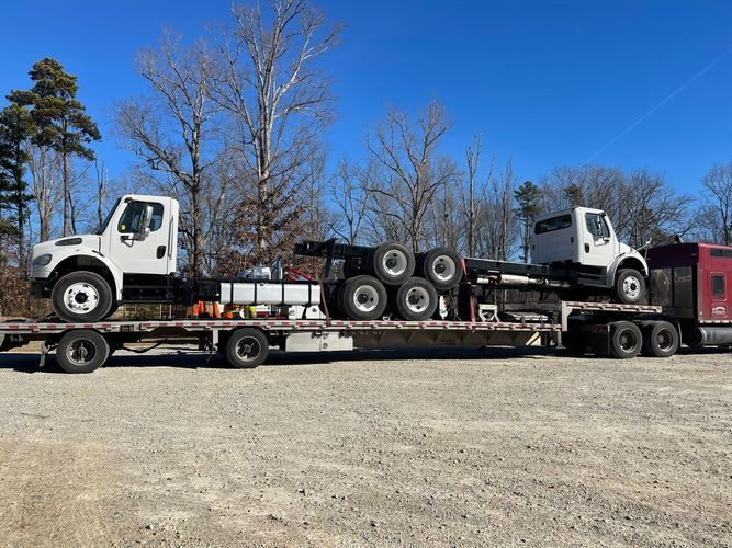 Two white truck cabs on a flatbed trailer, parked outdoors on a sunny day.