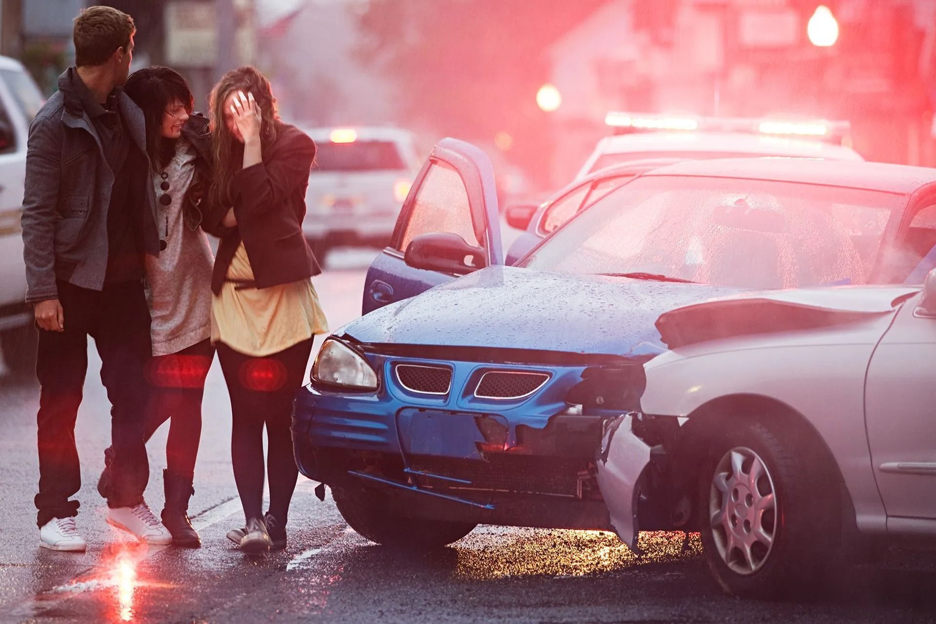 People at car accident scene; one woman cries, police lights flash.