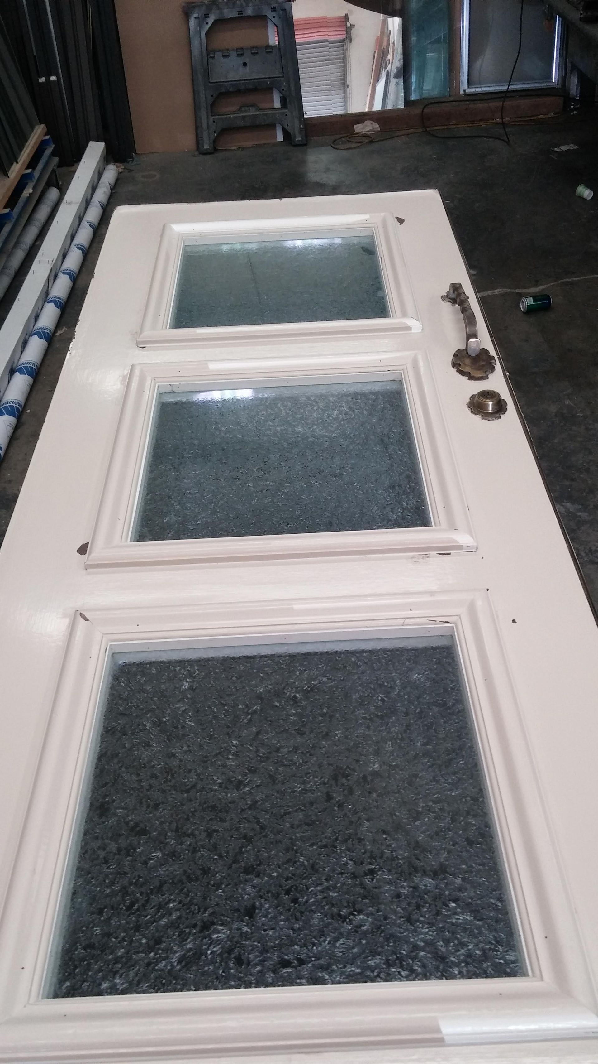 A white door with three windows is sitting on a concrete floor.